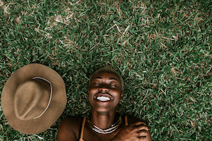Portrait Of A Beautiful Black Woman Smiling & Laying Down In The Grass.